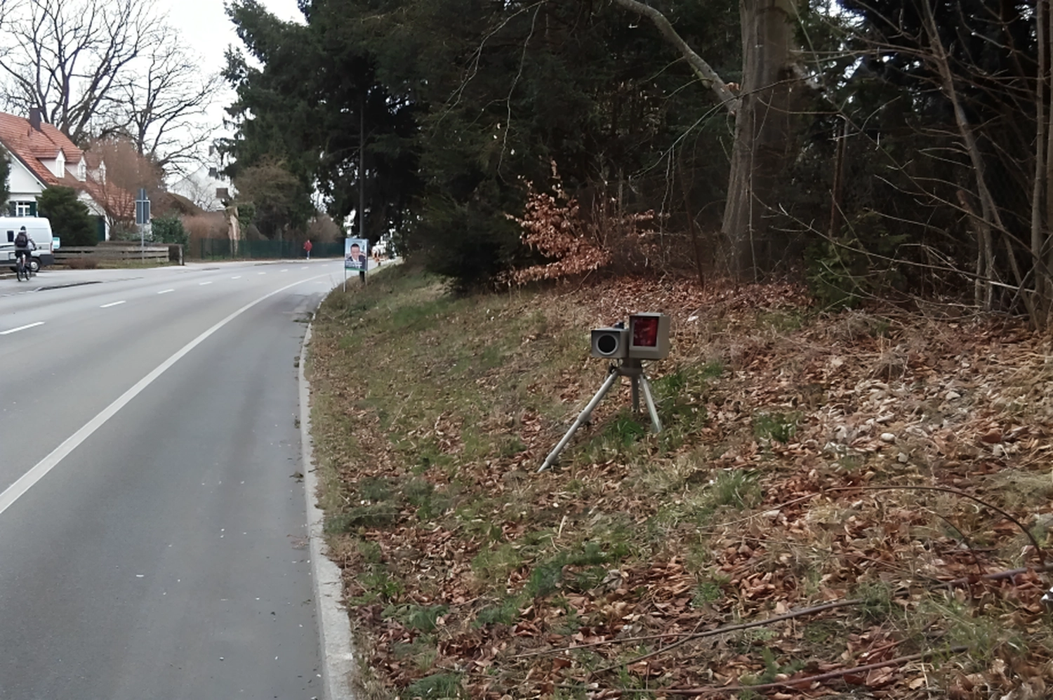 Radarrent GmbH - Verkehrsüberwachung - Radargeschwindigkeitskamera auf Stativ zur Überwachung des Verkehrs auf einer Vorstadtstraße neben einem Waldstück mit trockenem Laub