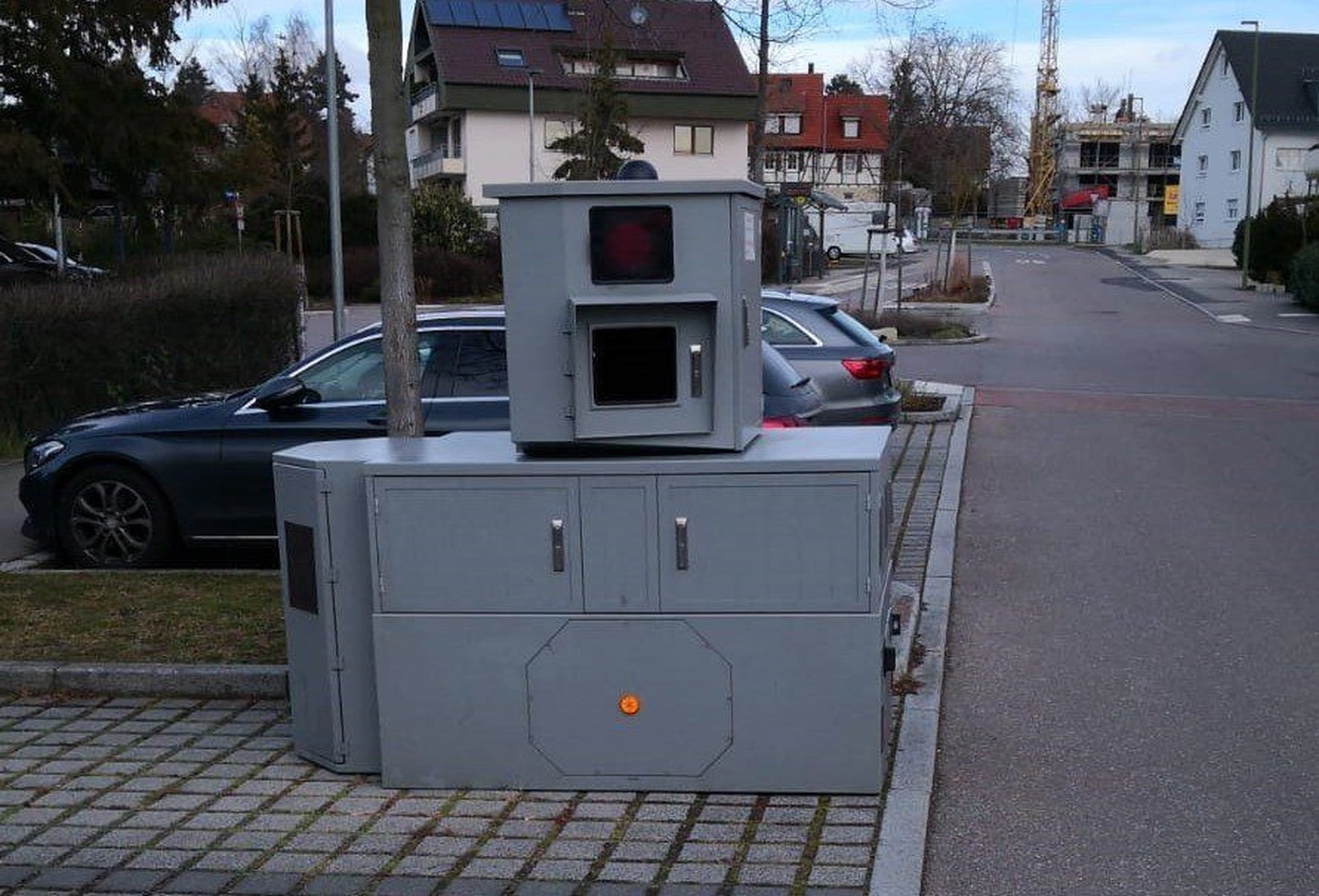 Radarrent GmbH – Verkehrsüberwachung  – Graue Verkehrsüberwachungskameraanlage, installiert auf einem Gehweg in der Nähe von geparkten Autos in einem Wohngebiet