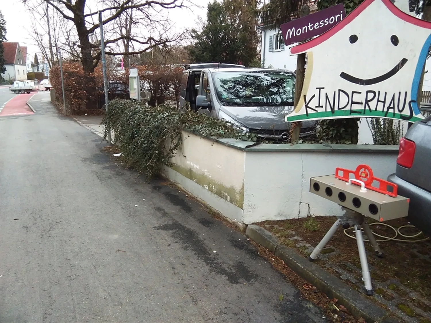 Radarrent GmbH - Verkehrsüberwachung - Straßenansicht mit einem Schild mit der Aufschrift Montessori Kinderhaus und einem Gerät auf einem Stativ in der Nähe des Bürgersteigs