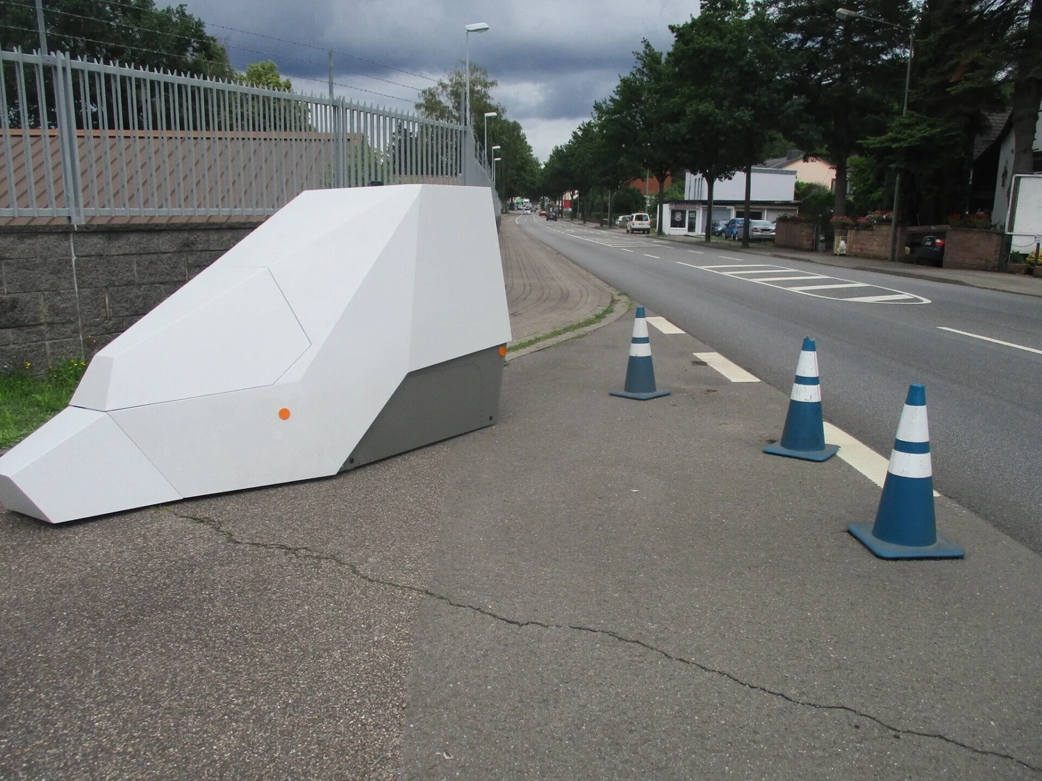 Radarrent GmbH - Verkehrsüberwachung - Großes weißes geometrisches, tierförmiges Objekt auf dem Gehweg neben drei blau-weißen Verkehrskegeln am Straßenrand